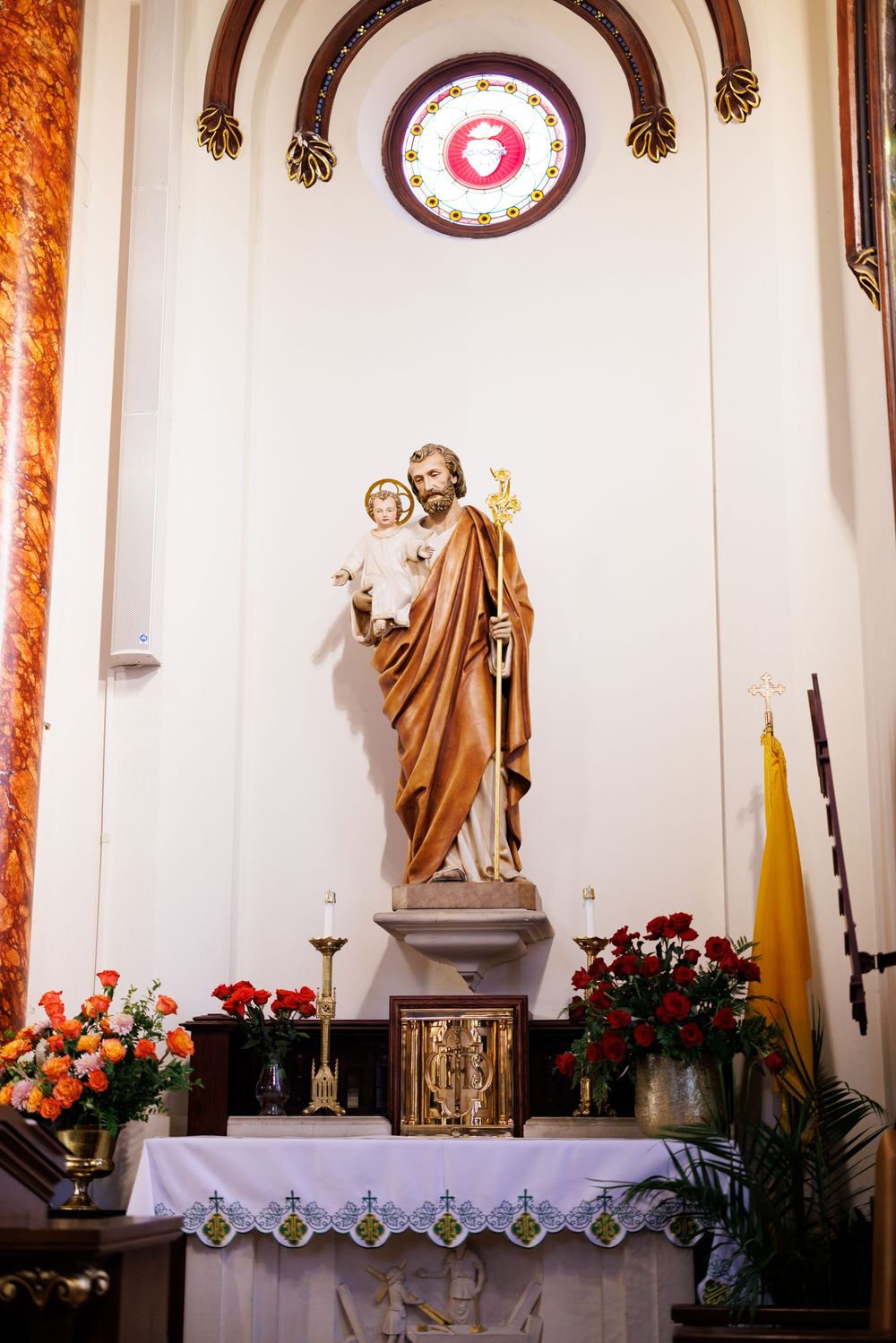 Religious statue adorned with red and orange flowers on church altar.