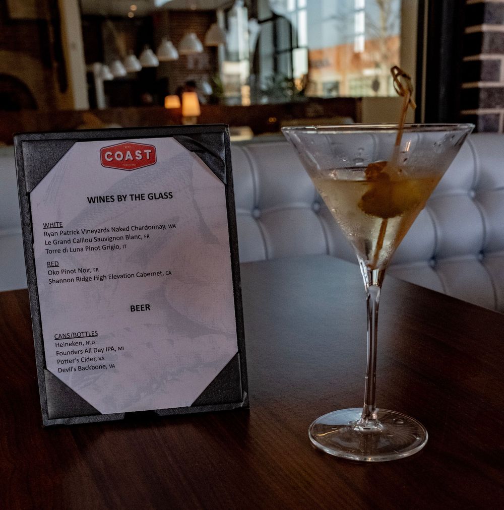 Martini cocktail with olive beside a Coast restaurant wines by the glass menu on a wooden bar.