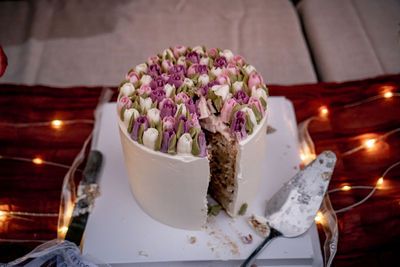 Elegant white cake topped with pink and purple tulips, partially sliced, surrounded by warm fairy lights.