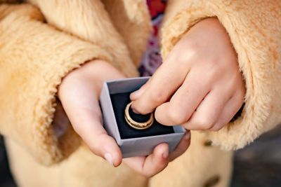 Child in fluffy coat holding a gray gift box with a gold ring inside.