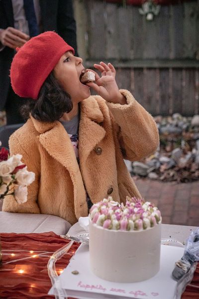 Woman in red beret and tan teddy coat eating cake at a decorated outdoor birthday celebration.