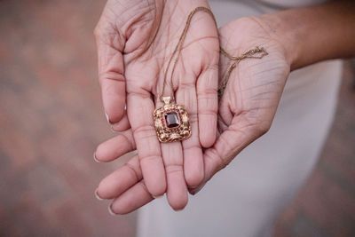 Hands holding a vintage gold pendant necklace with a dark gemstone center on a delicate chain.