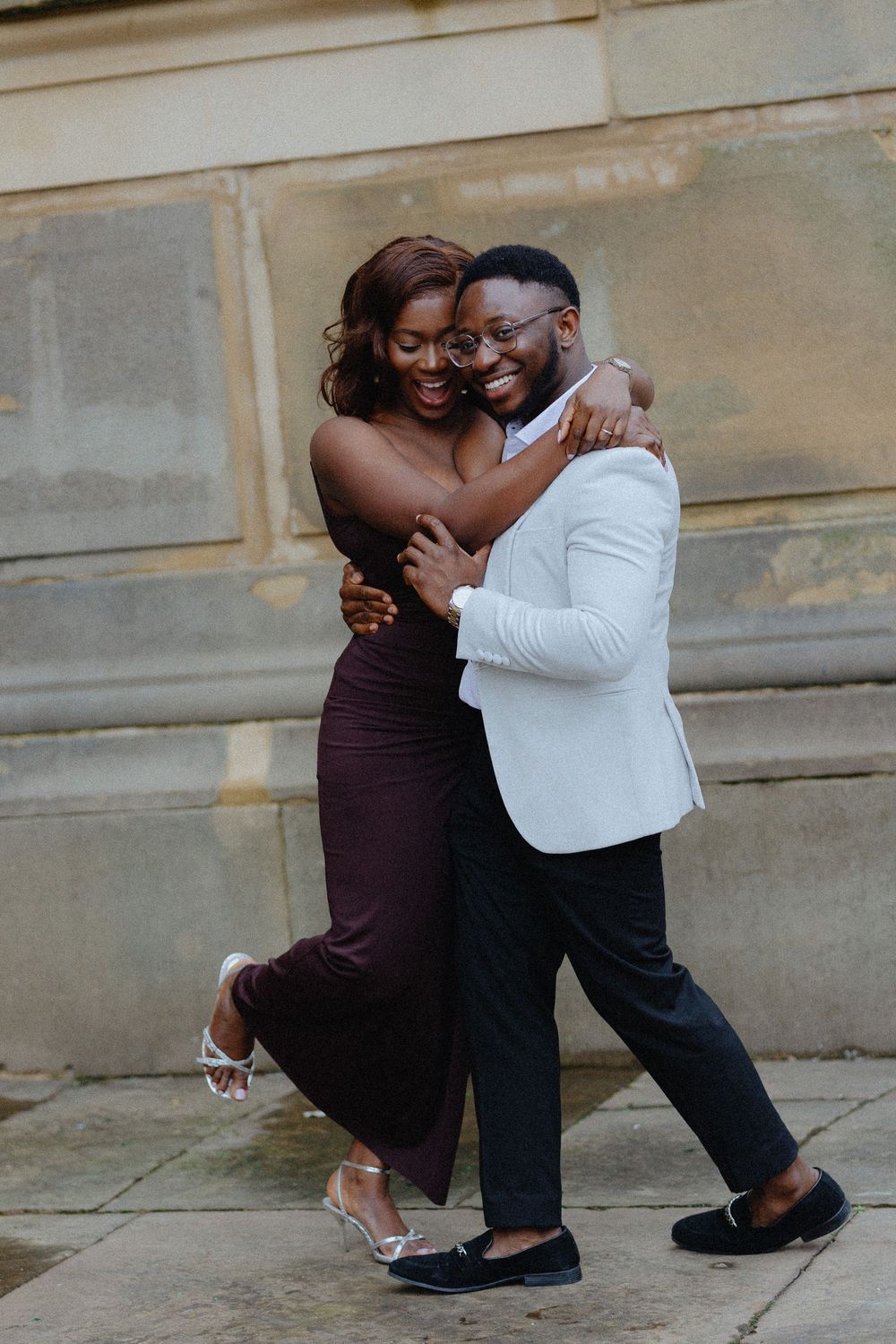 A couple shares an intimate dance moment together on stone steps, wearing brown and white outfits.