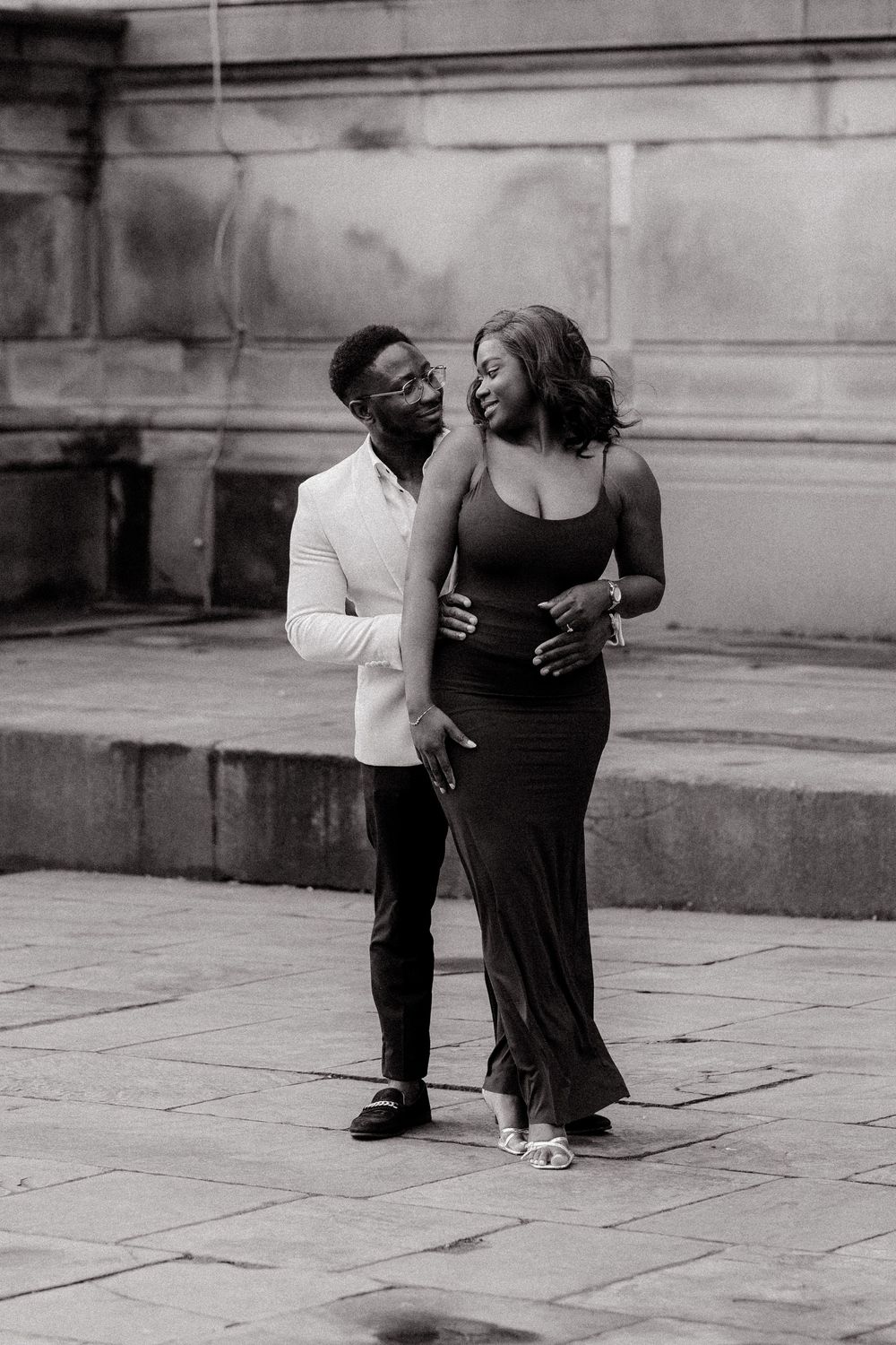 A romantic black and white photo of a couple in formal attire sharing an intimate moment on stone steps.