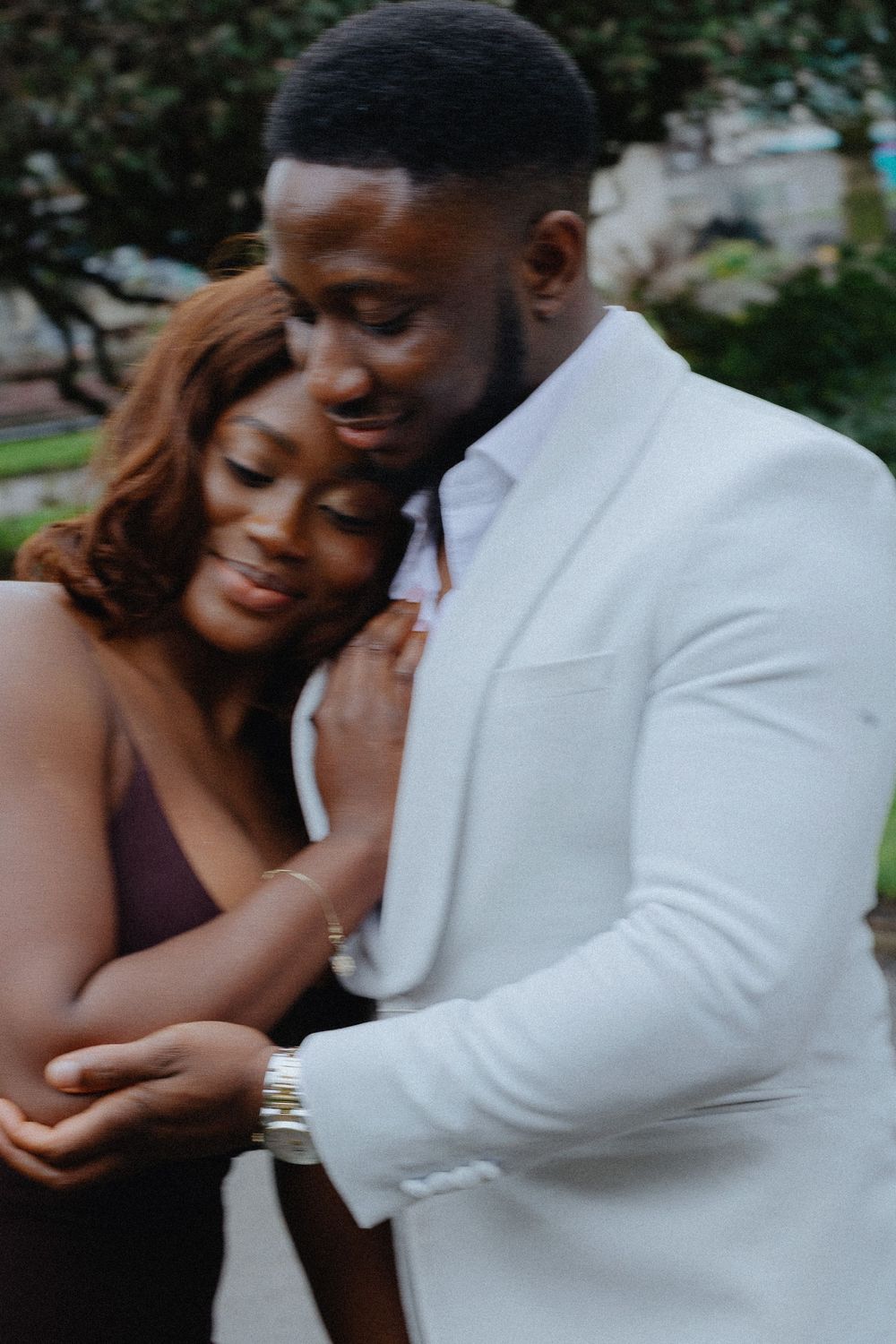 A romantic couple embracing in an outdoor setting wearing formal attire.