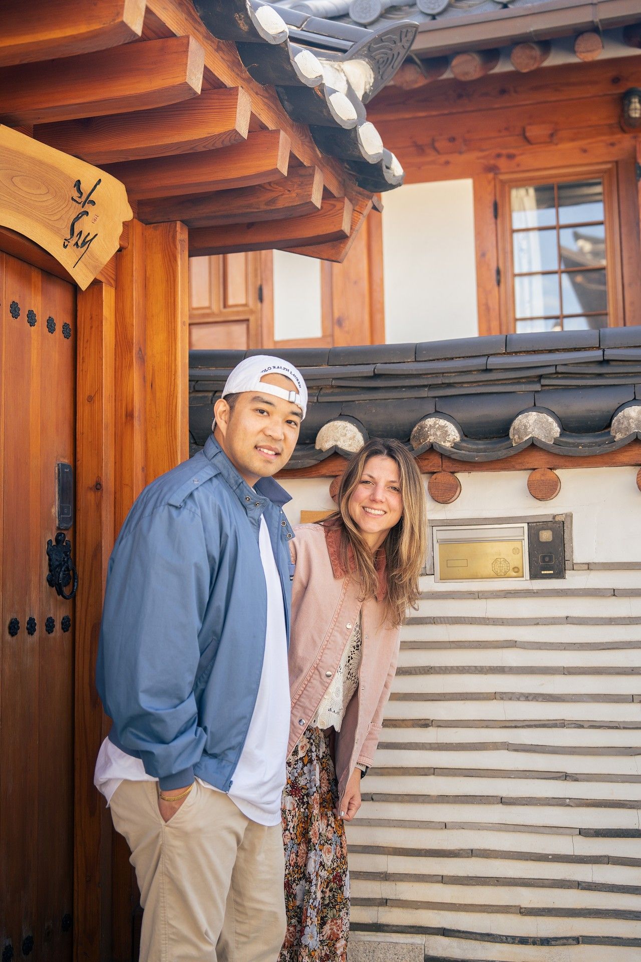 Couple smiling together while visiting a traditional Korean hanok house with white walls and wooden beams.