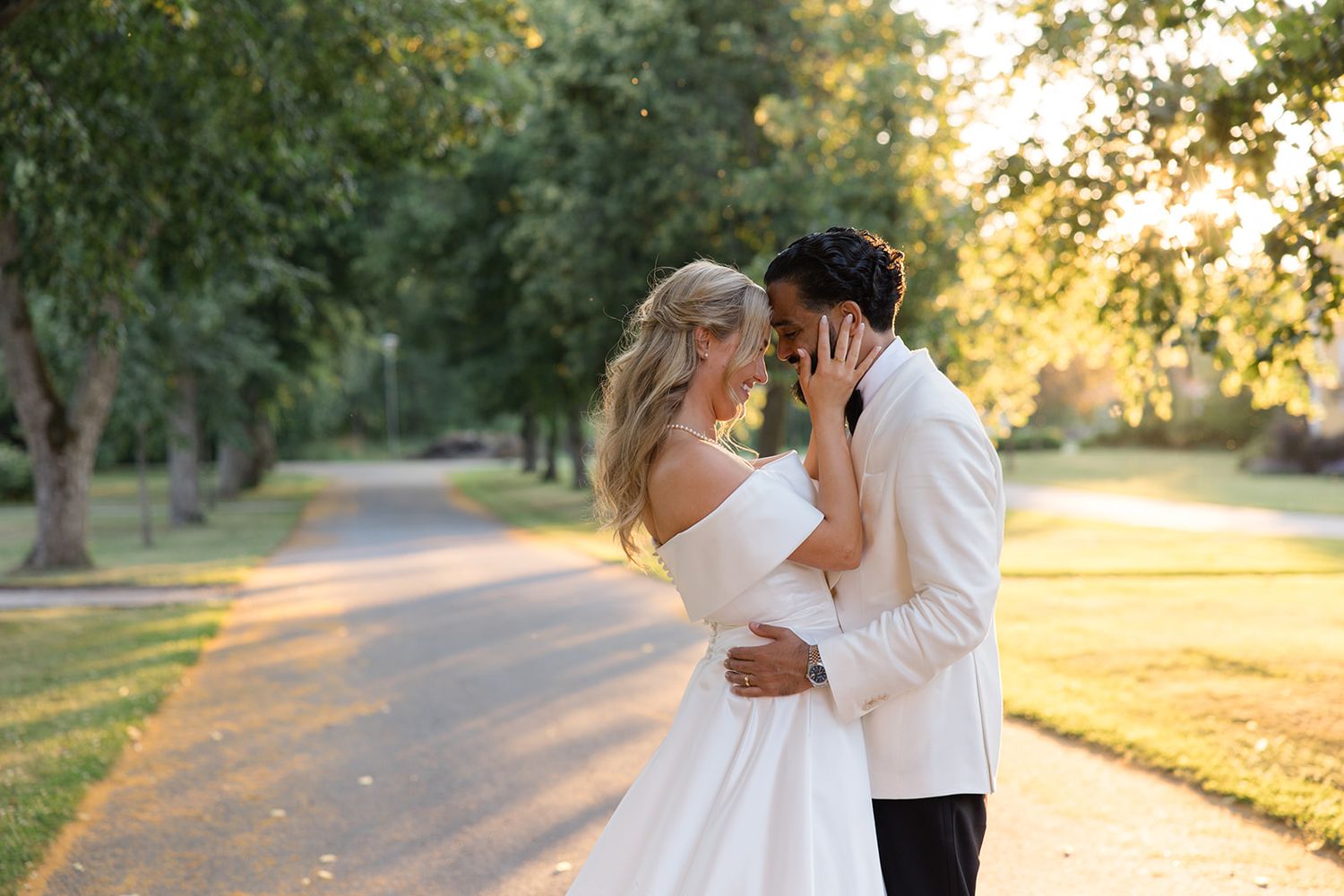 A couple shares romantic moments at sunset in a tree-lined park pathway with golden light filtering through.