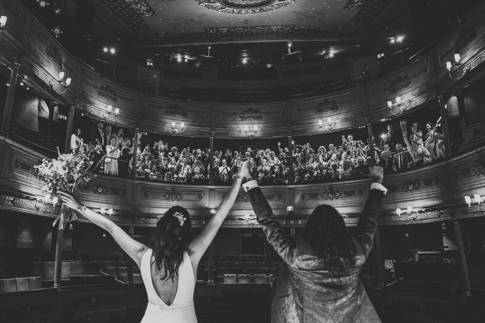 A panoramic view of a packed concert venue with stage lights illuminating a dark theater during a live performance.