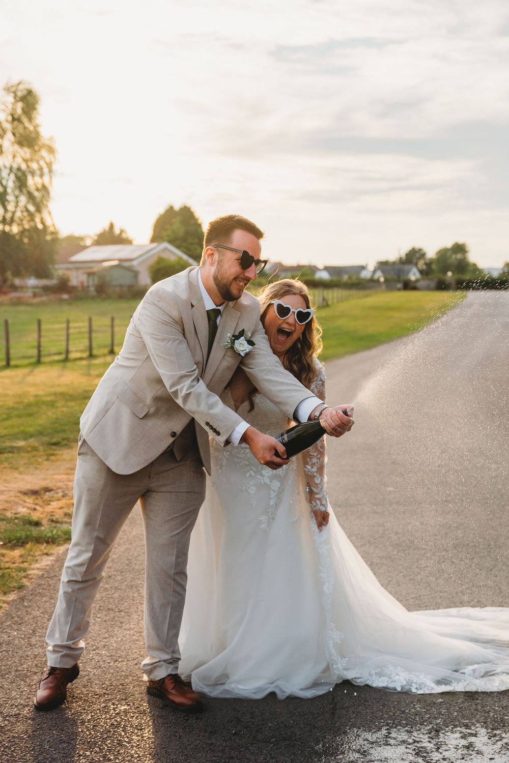 A couple in wedding attire poses playfully on a rural country road at sunset.