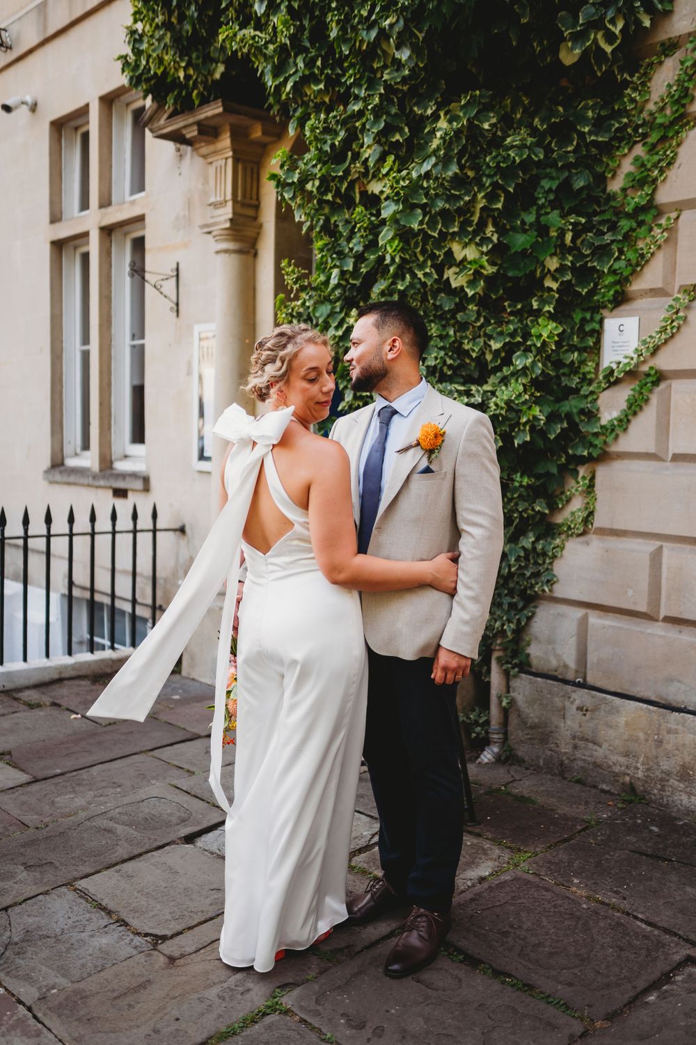 A romantic wedding couple shares an intimate moment against a stone building with ivy growing on the walls.