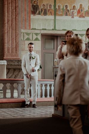 Series of artistic shots showing a groom in cream suit inside a church with decorative wall murals.