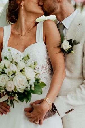 Intimate wedding photography details showing white dress lace, cream suit, and floral bouquet.