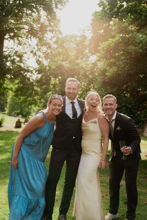 Wedding party in blue and black attire laughing together in a sun-drenched garden.