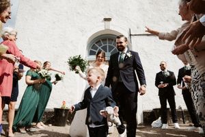Wedding party and guests celebrating with animated poses against white building exterior.