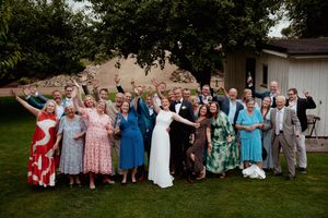 Large group wedding photo with guests in colorful attire gathered outdoors.