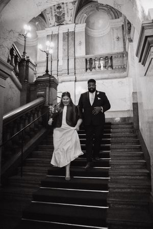A couple descends an elegant staircase in a historic building during their wedding.