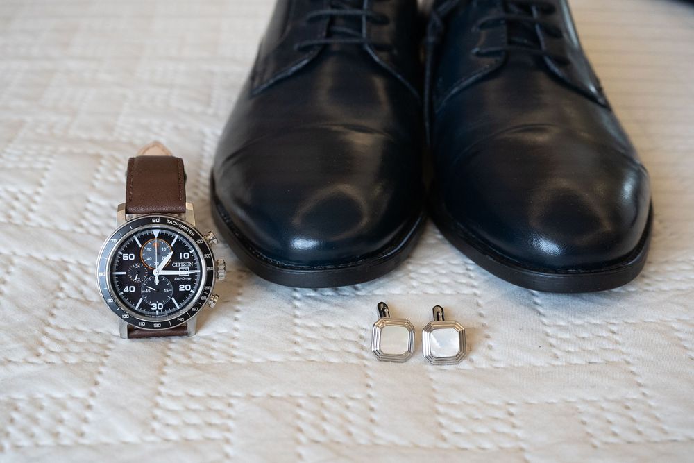 Black formal dress shoes and accessories arranged on white textile.