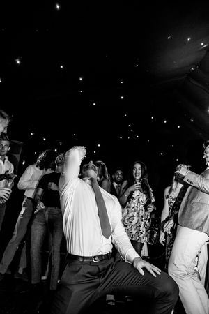 Black and white photo of people dancing and celebrating at a lively nighttime party on a dance floor.