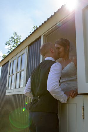 A romantic sunlit moment between a couple outside a rustic building with white walls.