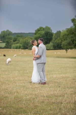 A couple shares a romantic moment in a pastoral field with hay bales and sheep scattered in the background.