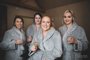 Bridal party wearing matching gray robes pose while holding champagne glasses before the wedding.
