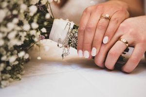 Close up of hands holding a wedding ring with delicate decor and floral arrangements in the background.