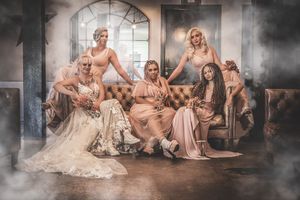 Wedding party lounges on vintage furniture in a moody studio setting with dramatic fog effects.