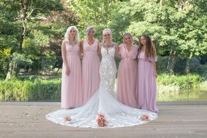 Wedding party in pink bridesmaid dresses posed together outdoors in garden setting.