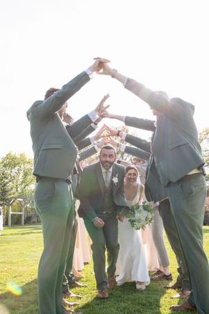 Wedding guests form an arch tunnel with their arms raised during an outdoor celebration.