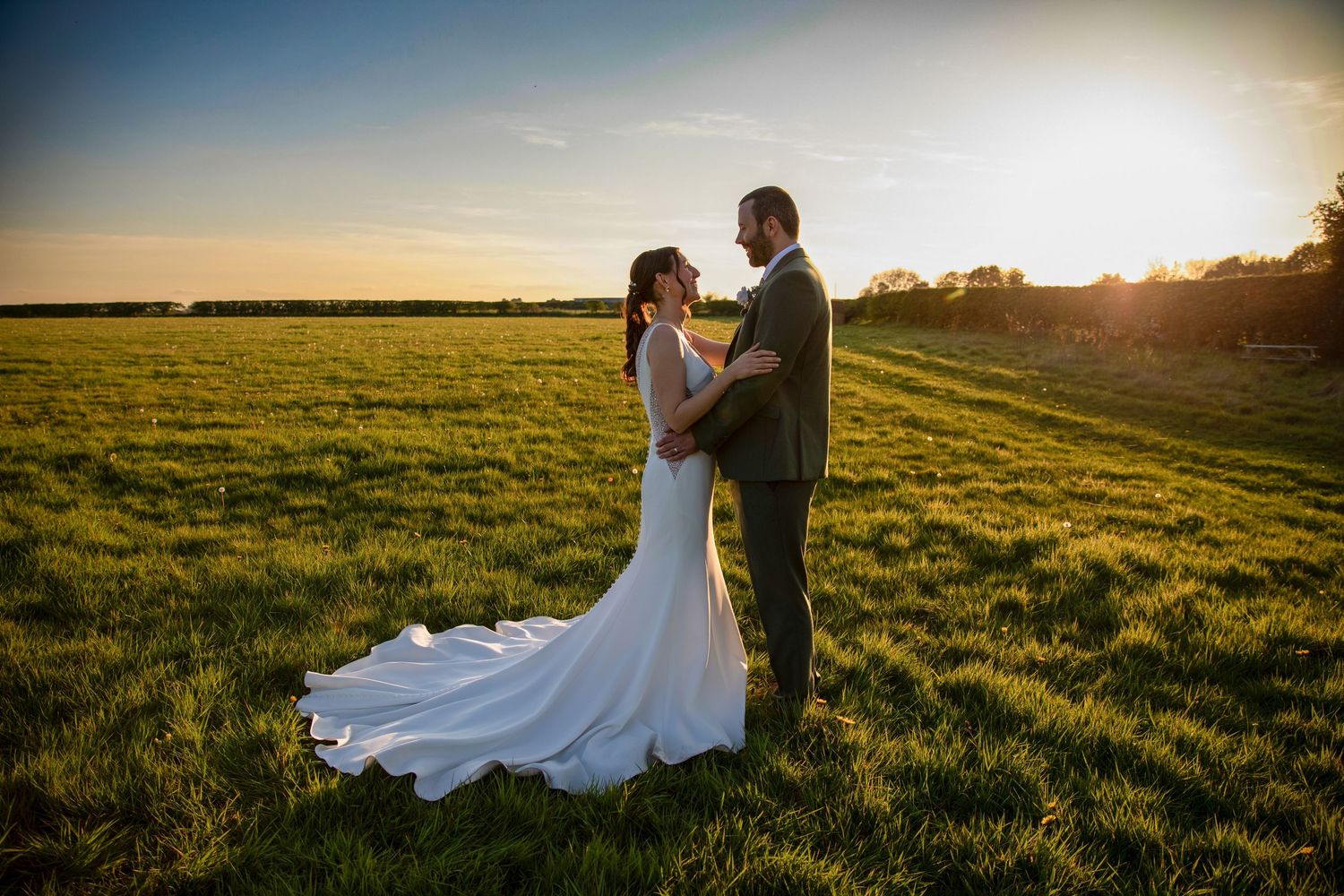 Romantic sunset portraits in a vast green field during a wedding celebration.