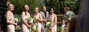 Wedding party members laughing while standing together outdoors during photo session.