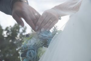 Elegant wedding ring detail shot with soft sunlight filtering through white fabric and flowers.
