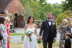 Guests gather outdoors during a spring wedding celebration near a brick building.
