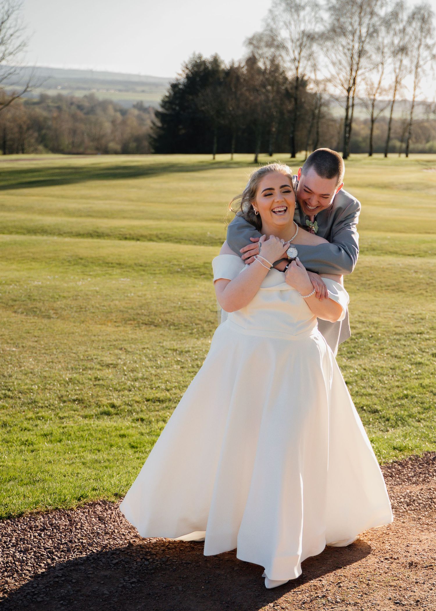 A joyful wedding couple embraces on a sunny golf course in Carluke, Scotland.