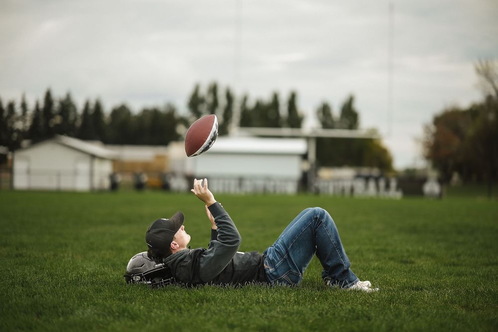 A person lies in a grassy field looking up at the sky on a cloudy day.