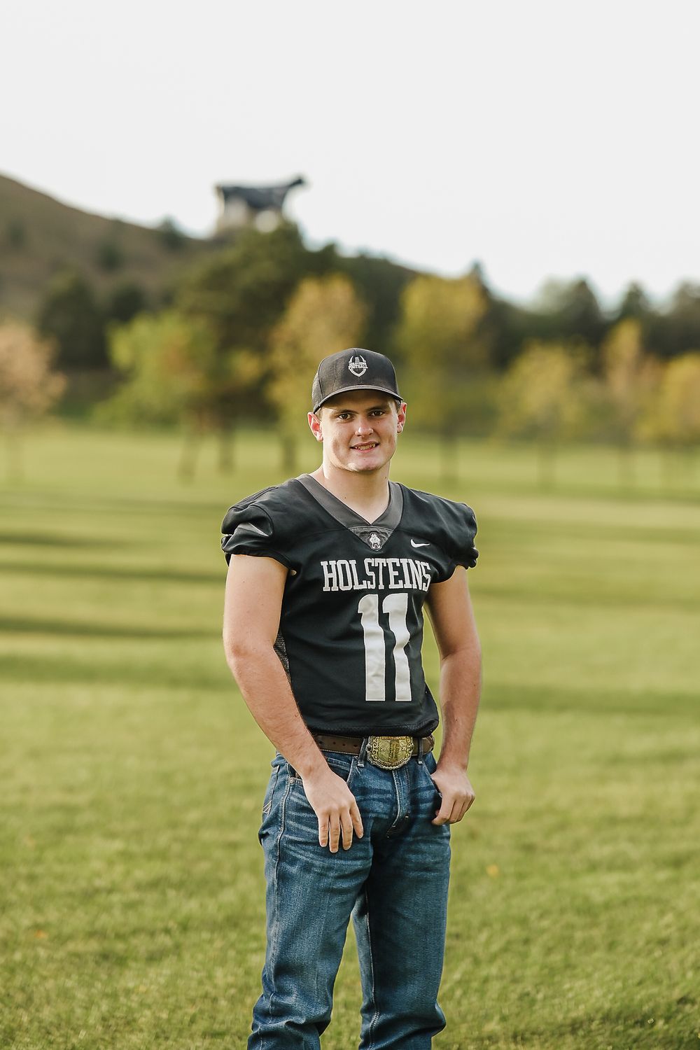 A young child in a black t-shirt and jeans stands confidently in a grassy field on a sunny day.