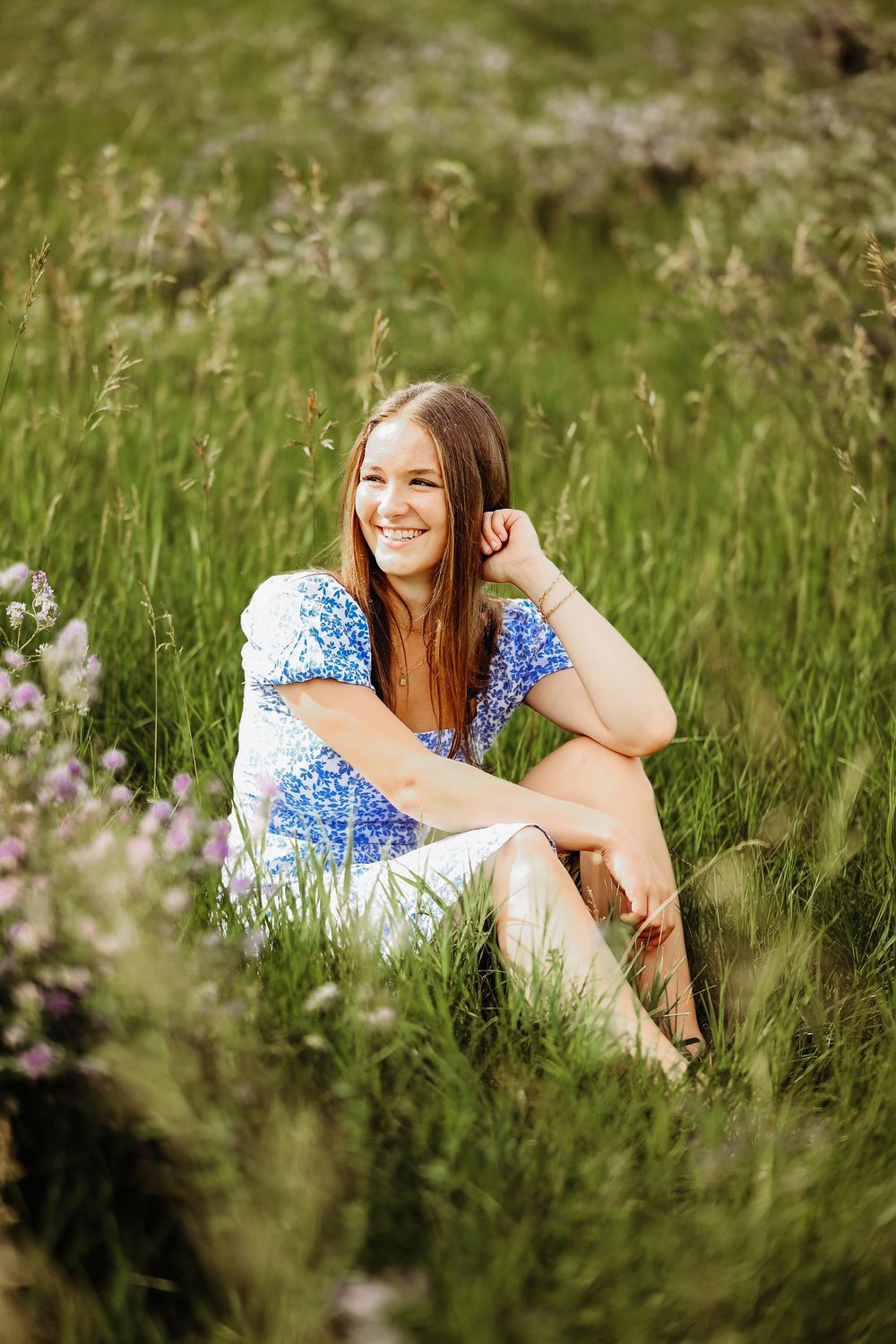 A person in a blue polka dot dress relaxes in a summer meadow filled with wildflowers and tall grass.