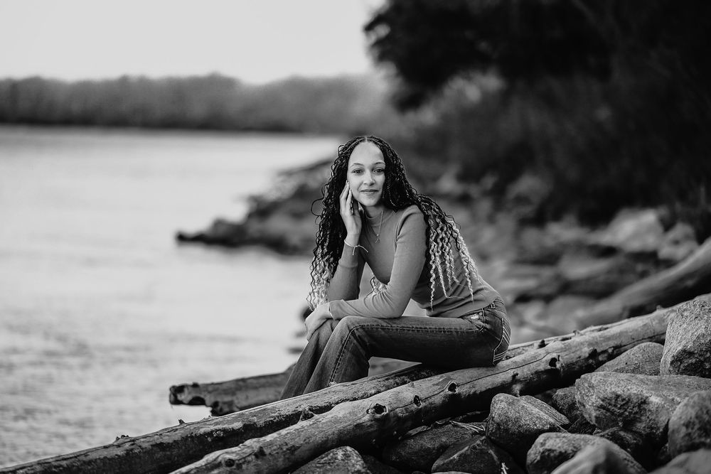 A black and white artistic portrait of someone lying on a beach with driftwood in a dramatic pose.