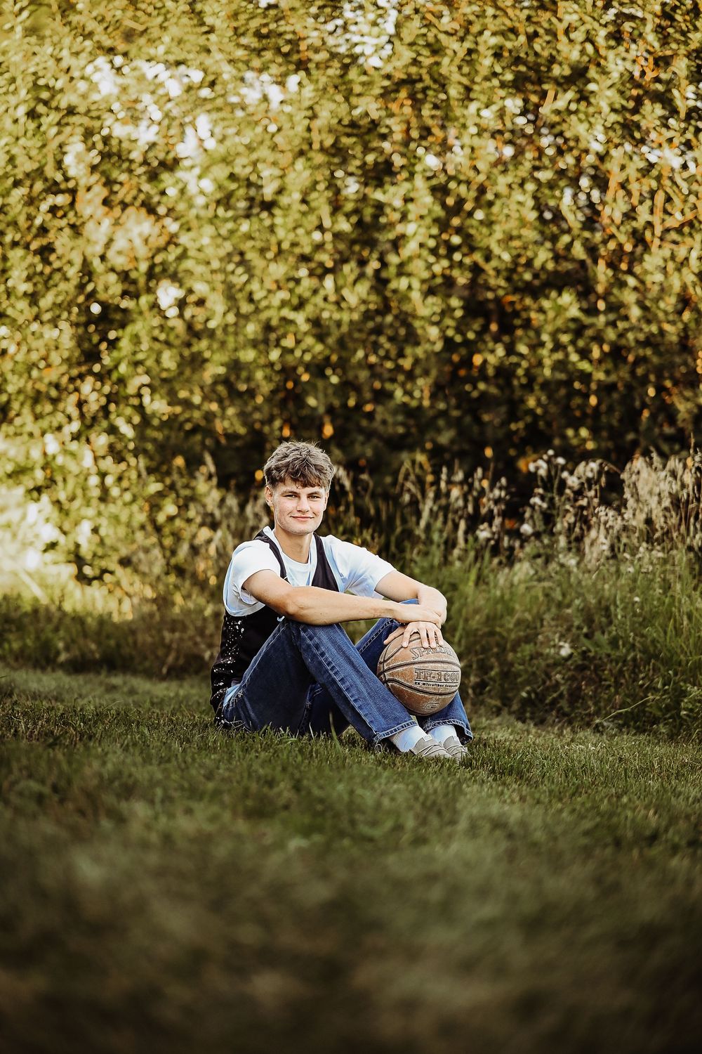 A basketball player sits thoughtfully in the grass with autumn foliage creating a golden backdrop.