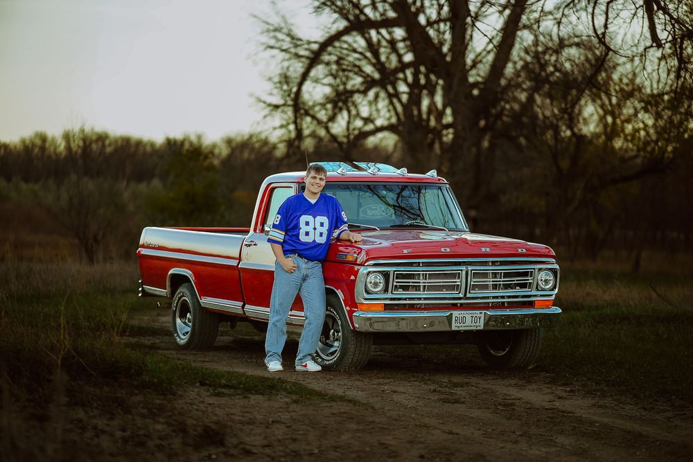 A romantic couple in blue outfits poses with a vintage red and white pickup truck at sunset.