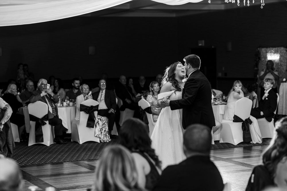 A black and white panoramic view of couples dancing at a formal event with tables and chairs in the background.
