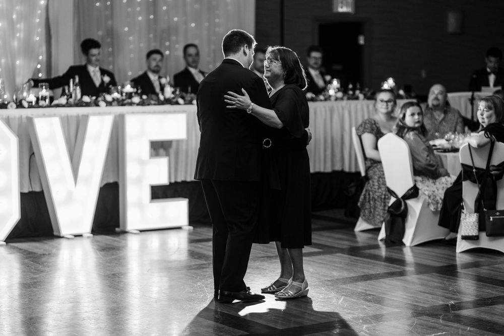 A couple dances elegantly on a ballroom floor during a formal event with LOVE letters and guests in the background.