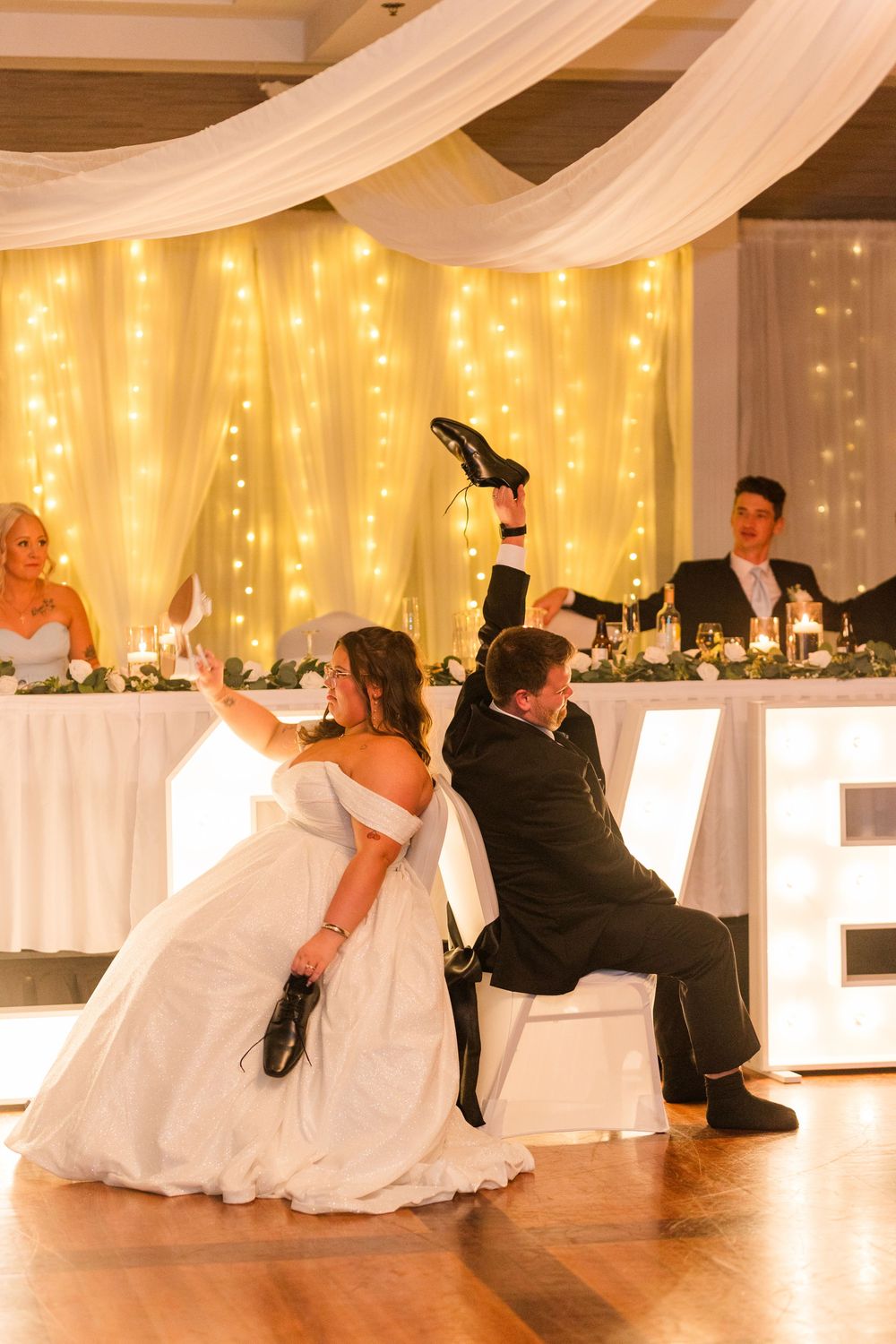 Wedding couple performs romantic dance dips sequence on illuminated reception dance floor with draped white fabric decor.