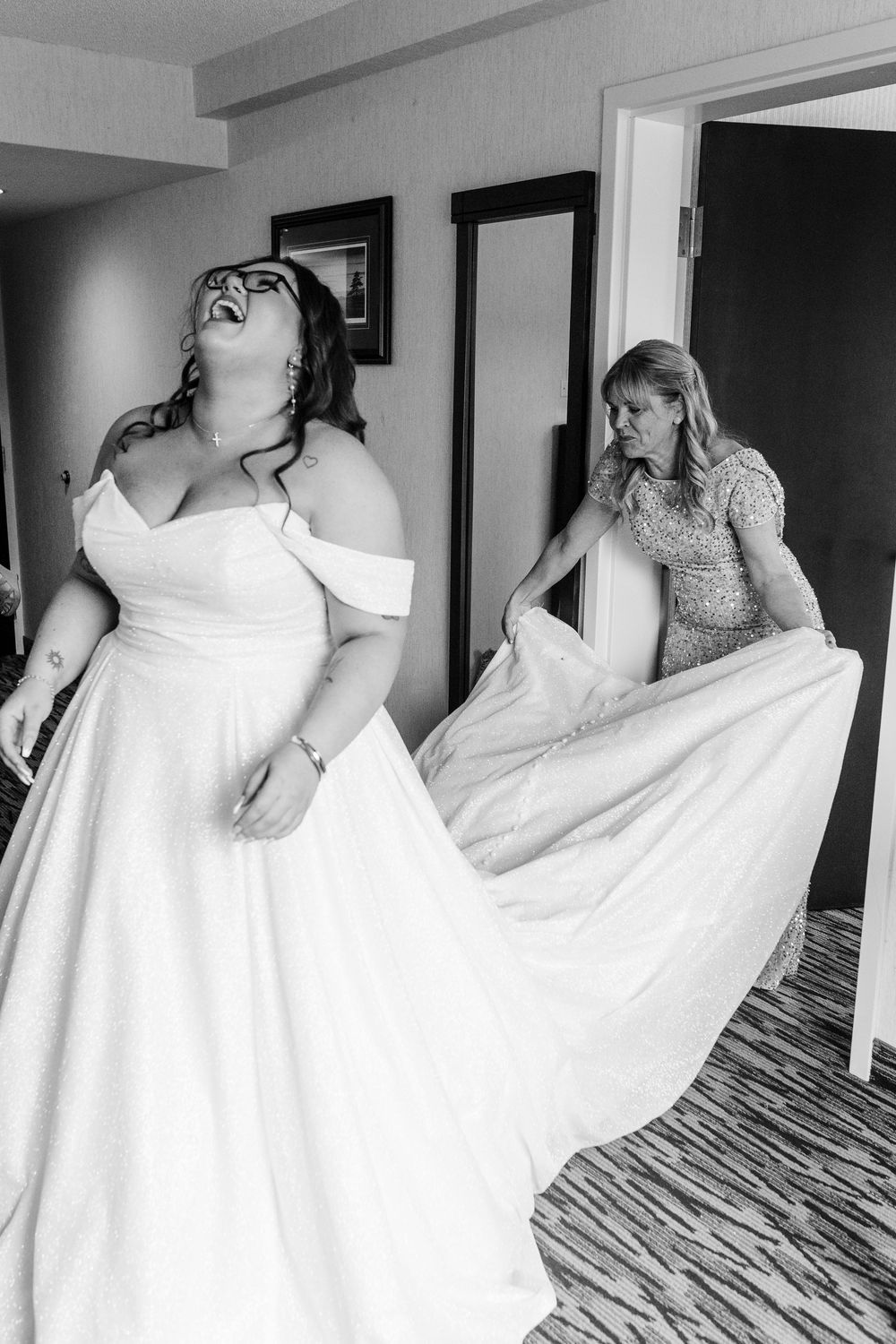 Two women in white dresses twirl and dance joyfully in a hotel room during wedding preparations.