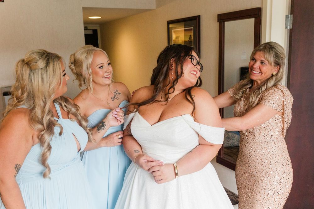 Wedding party members in blue and blush dresses help style the bride's hair and dress before the ceremony.