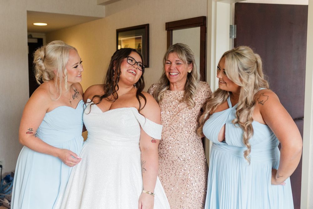 Bridesmaids in light blue gowns gather around bride wearing white dress during wedding preparations indoors.