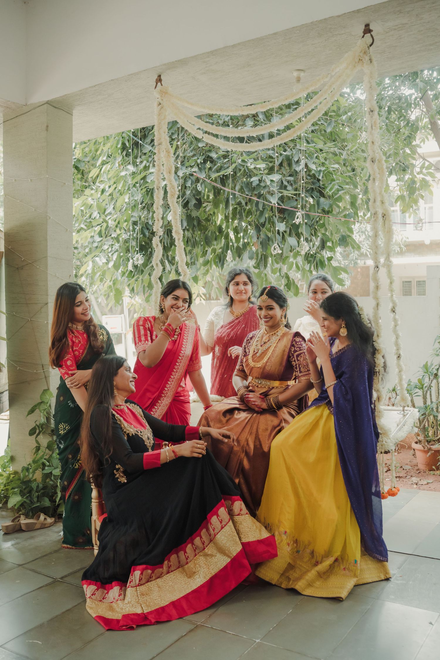 A group of women in colorful traditional Indian attire share joyful moments together while seated outdoors.