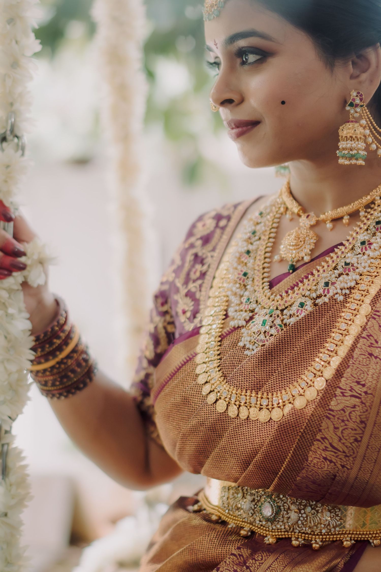 Close-up view of traditional Indian bridal jewelry featuring an ornate gold necklace and earrings with burgundy attire.