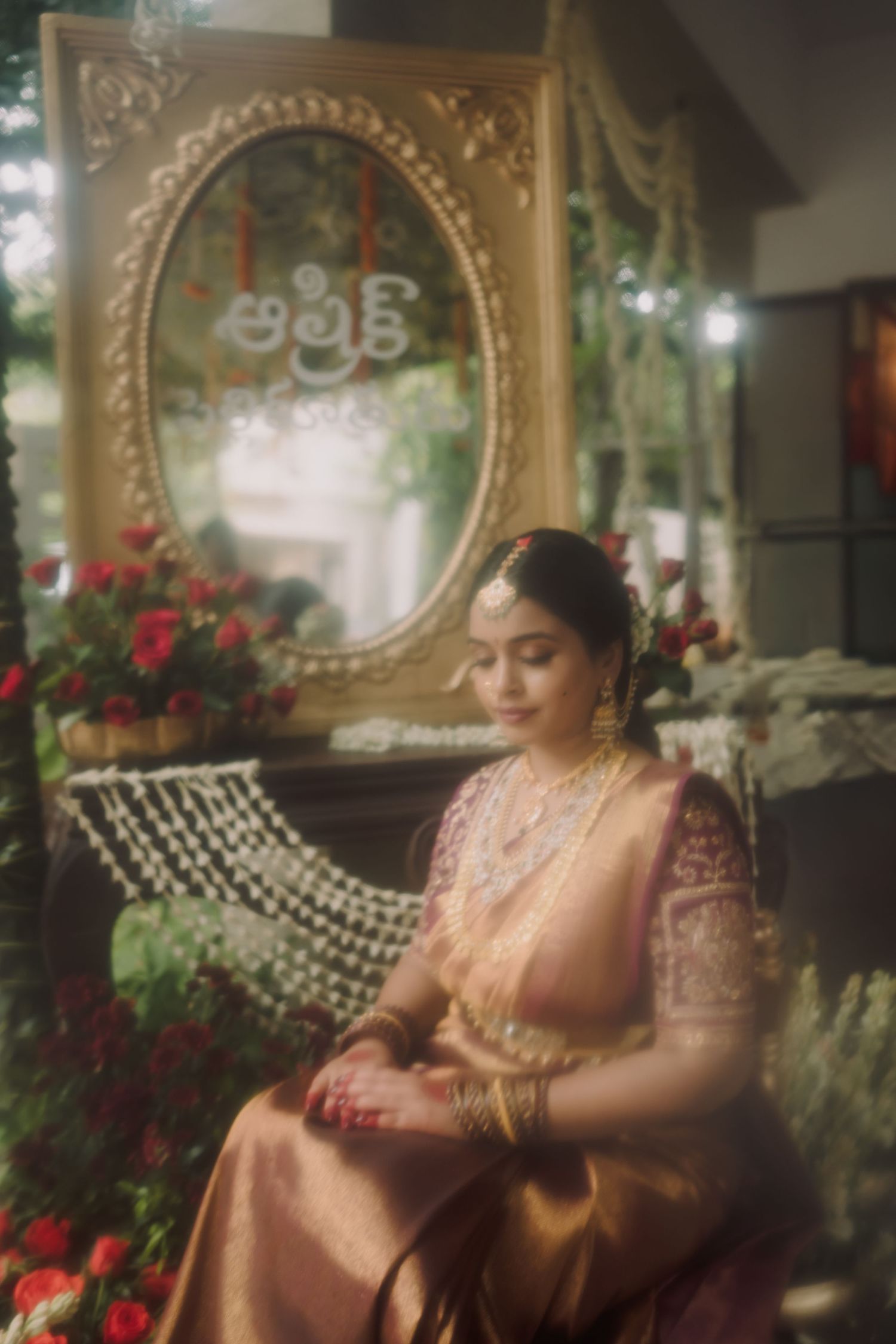 A person in traditional South Asian attire poses gracefully in an elegant setting with ornate mirrors and red roses.