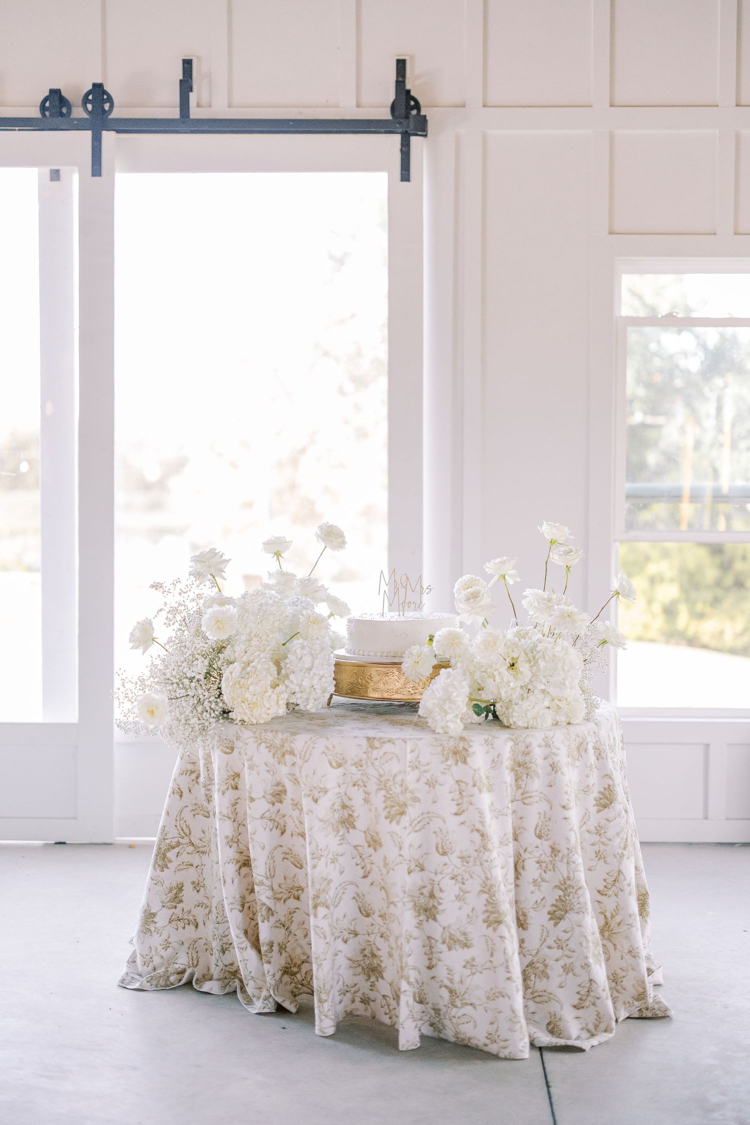 Elegant round tables set with floral patterned tablecloths in a bright white room with large windows.